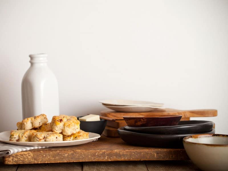 A plate of bacon gruyere and green onion scones next to butter, buttermilk, and plates.