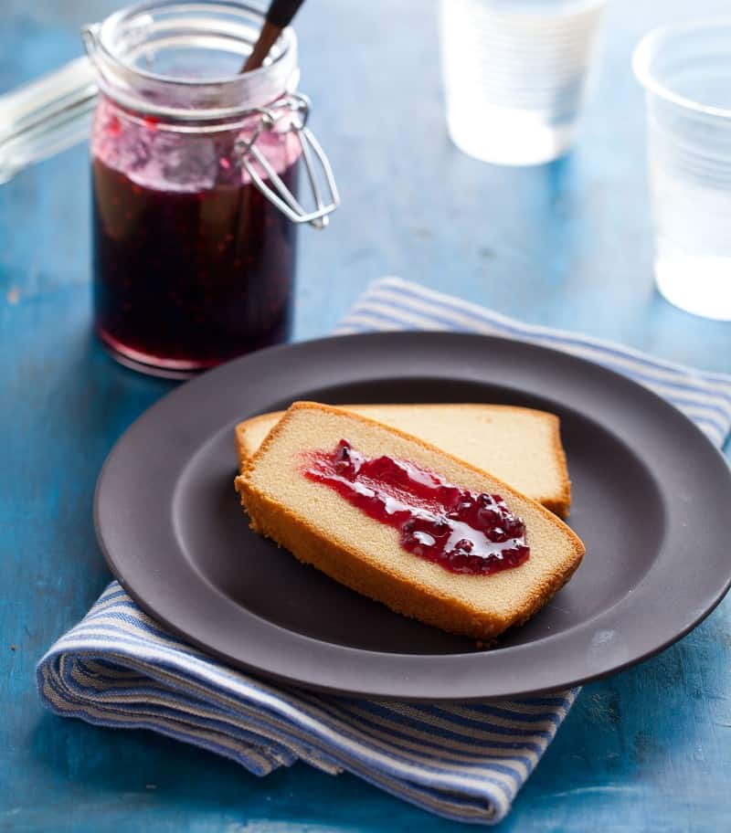 An open glass jar of simple blackberry jam and plate of bread with jam.