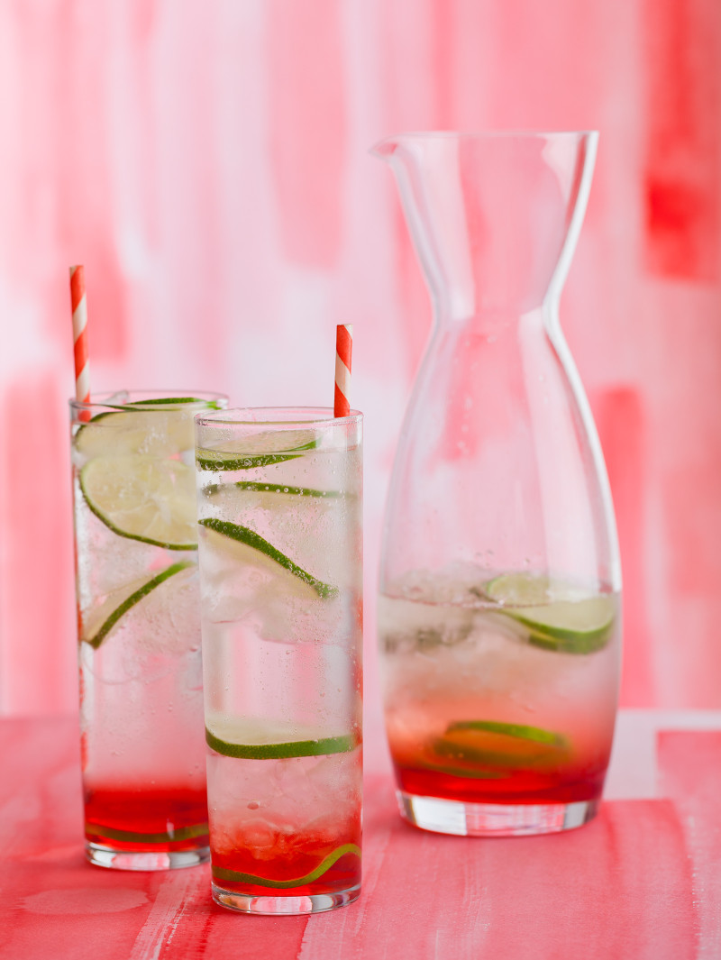 Sweet cherry gin and tonics with lime wheels and straws next to a half full carafe.