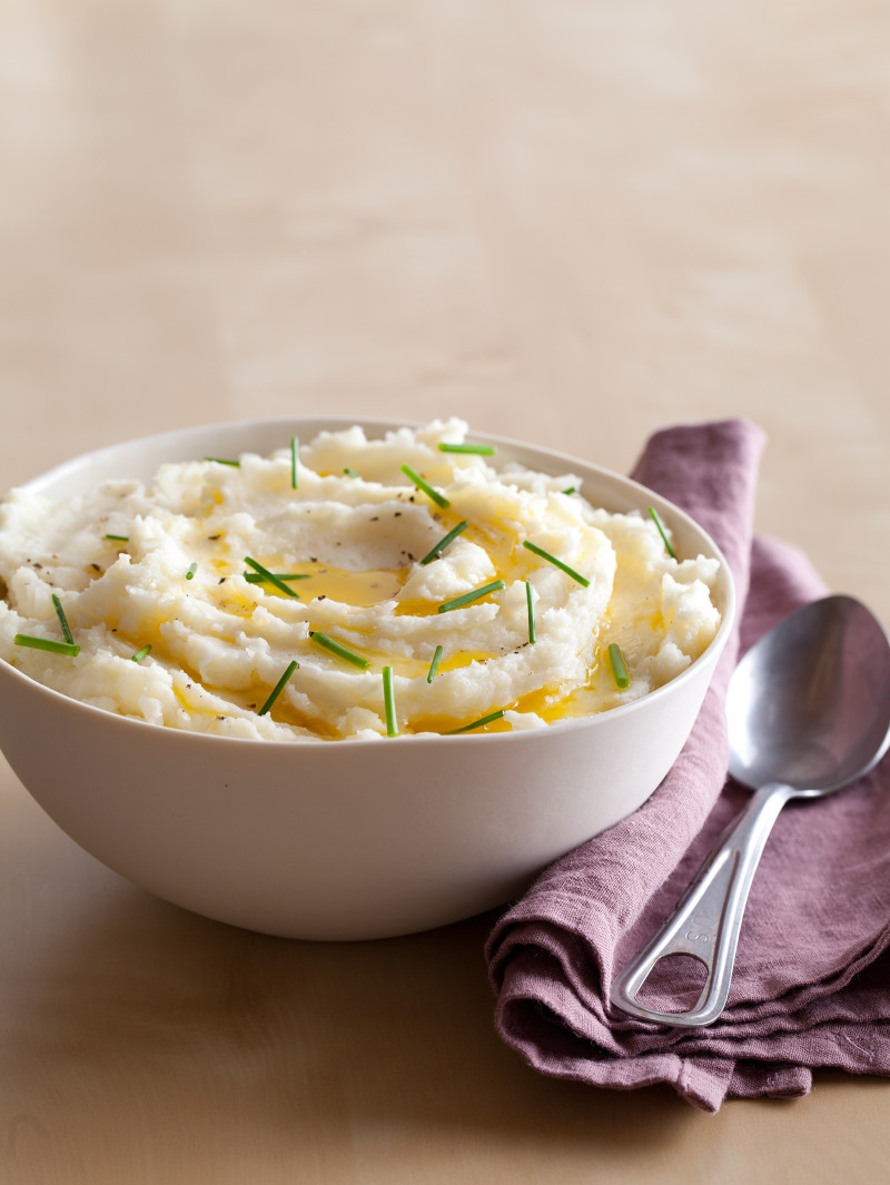 A bowl of mashed potatoes with butter and chives, a purple napkin, and a spoon.