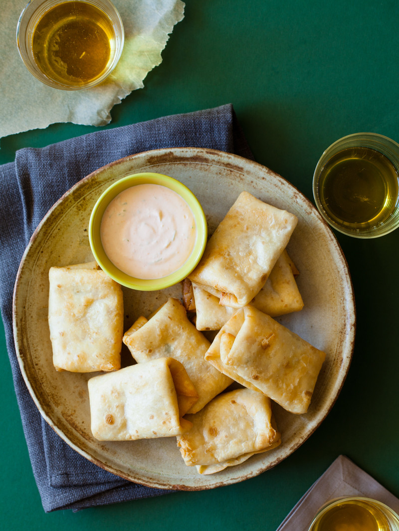 A plate of baby chimichangas with a bowl of sriracha lime dipping sauce.