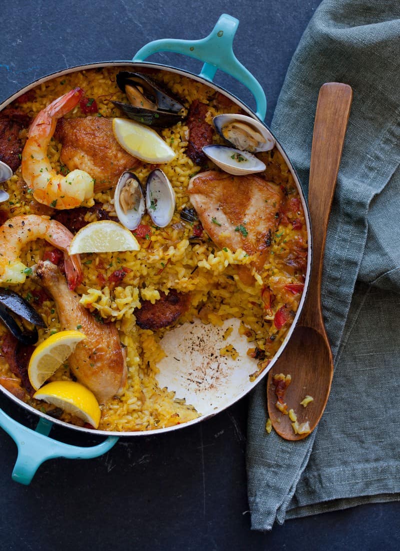 A pot of paella with a serving taken out and a wooden spoon.