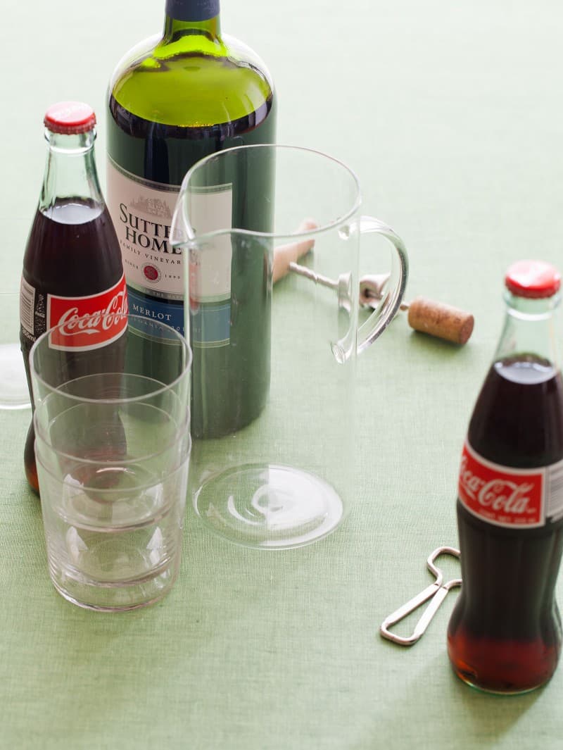 Ingredients for kalimotxo with a glass pitcher, empty glasses, and bottle openers.