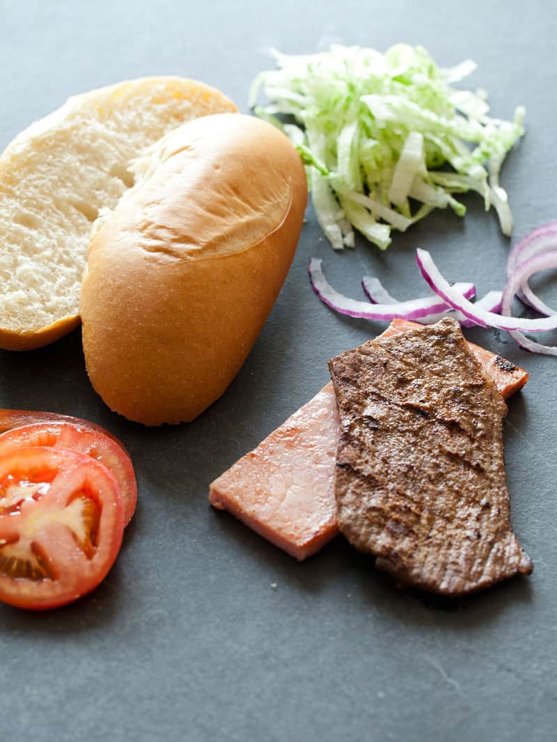 Chivito ingredients. Steak, ham, lettuce, bun, onions, and tomatoes.