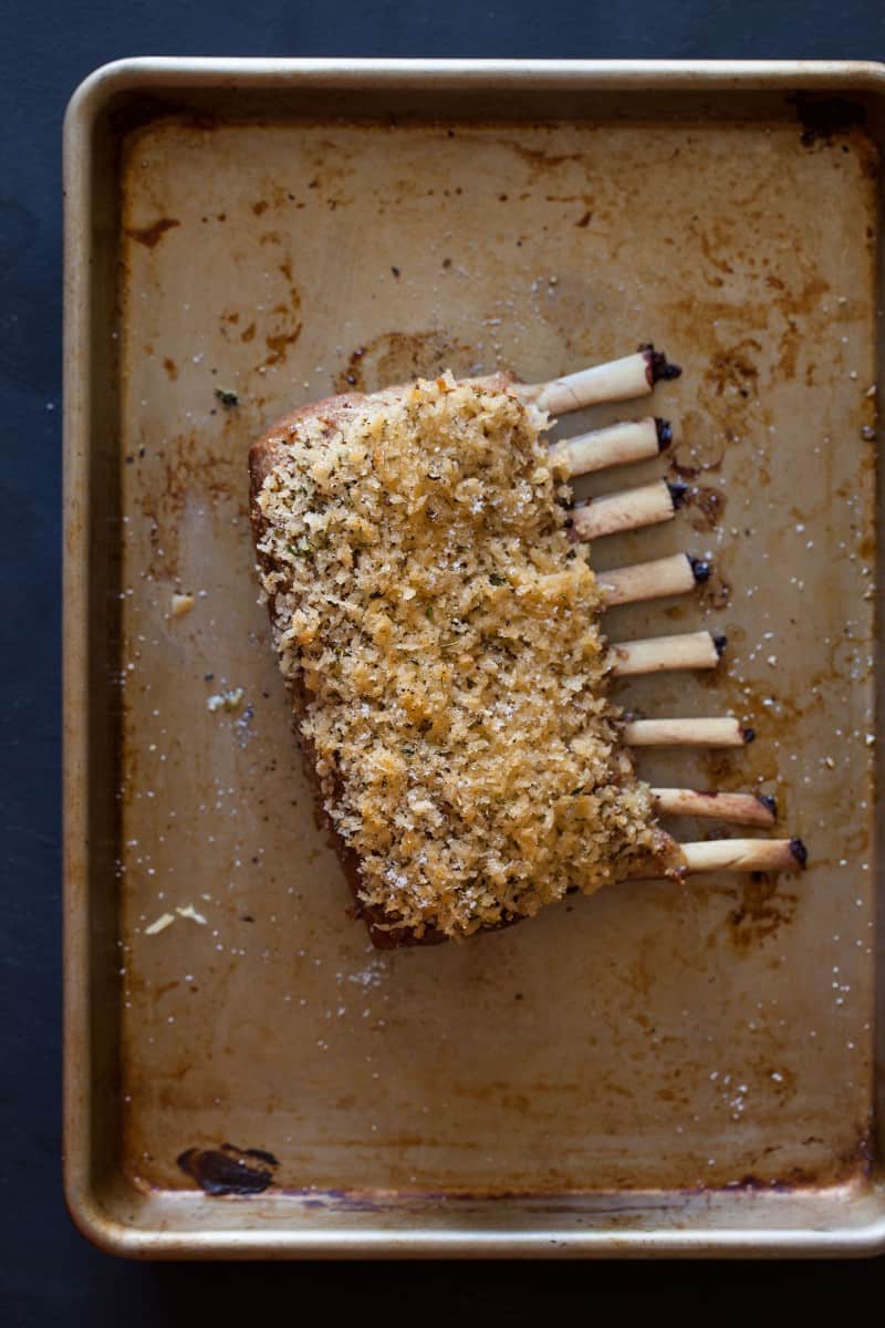 A seasoned and breaded rack of lamb on a sheet pan.