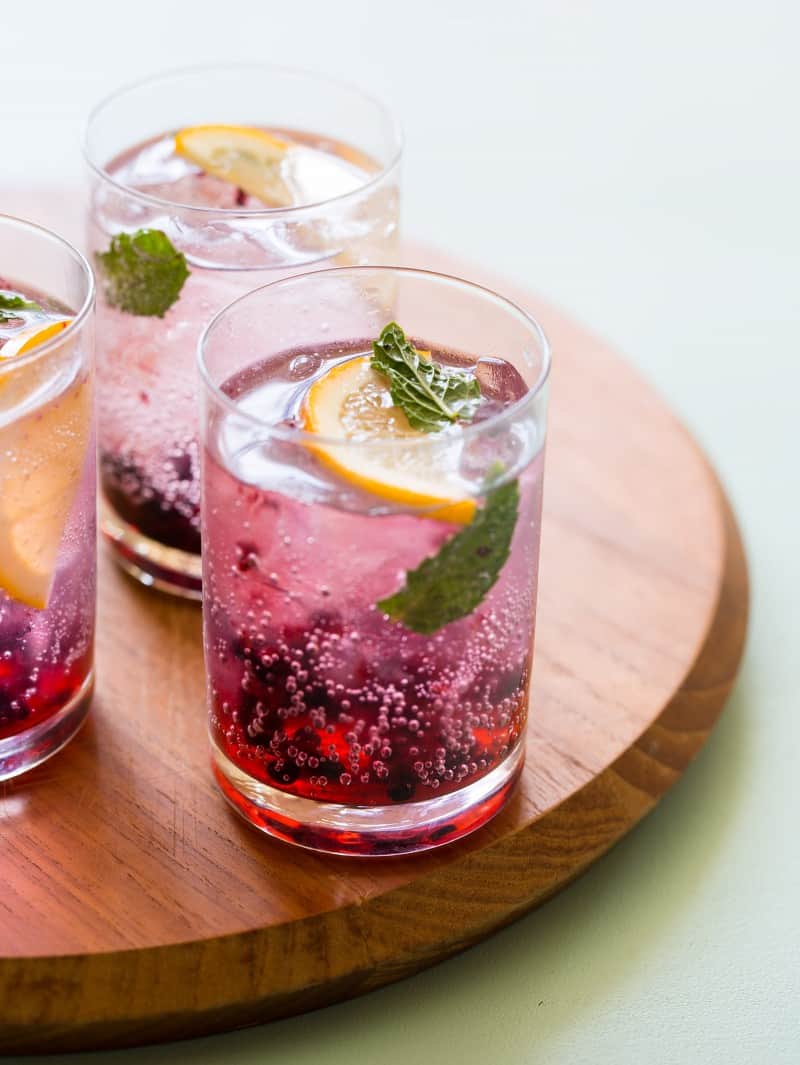 A close up of blackberry and meyer lemon gin and tonics on a wooden board.