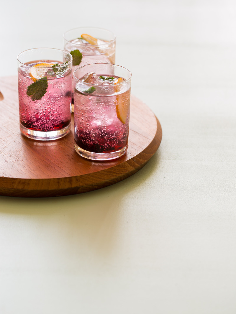 Glasses of blackberry and meyer lemon gin and tonics on a wooden board.