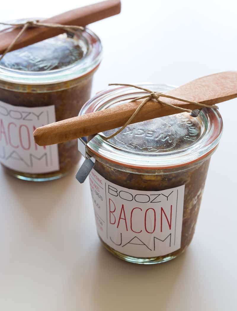 A close up of jars of bacon jam with printed labels and wooden knives attached.