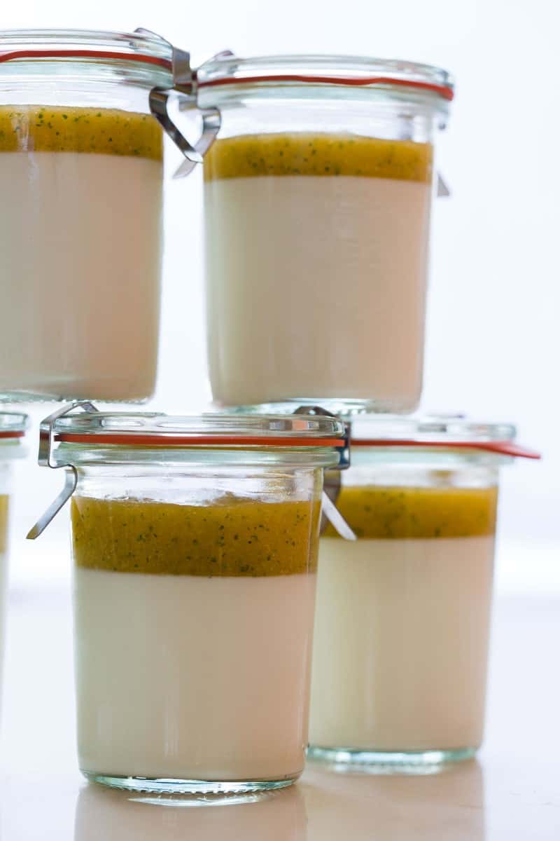 A close up of glass jars of vanilla bean panna cotta with mango coulis.