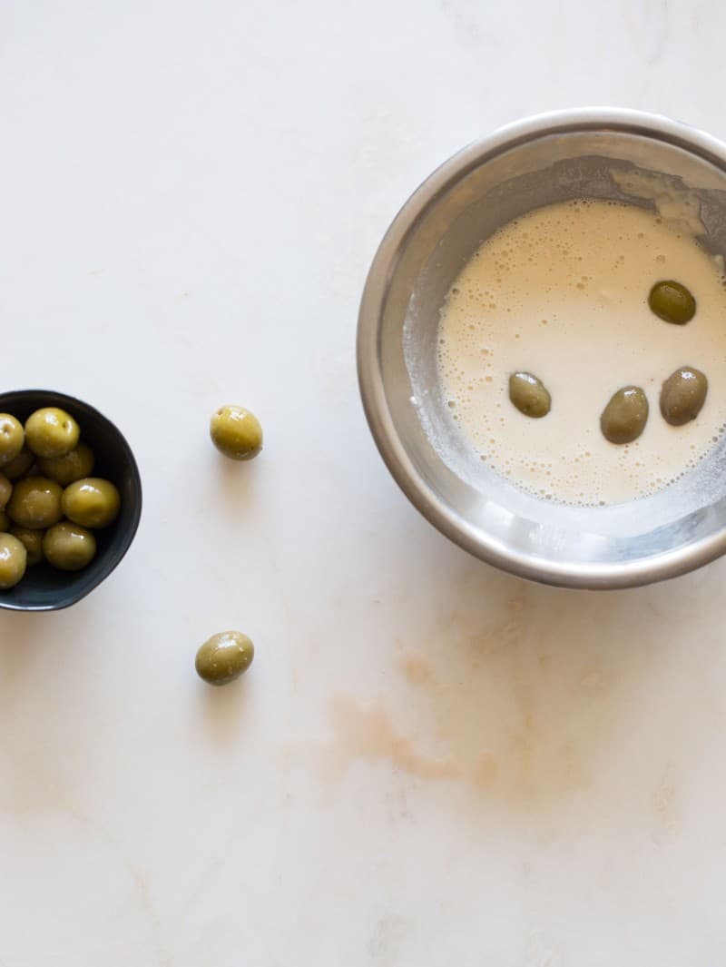 A small bowl of olives next to a larger bowl of olives in beer batter.