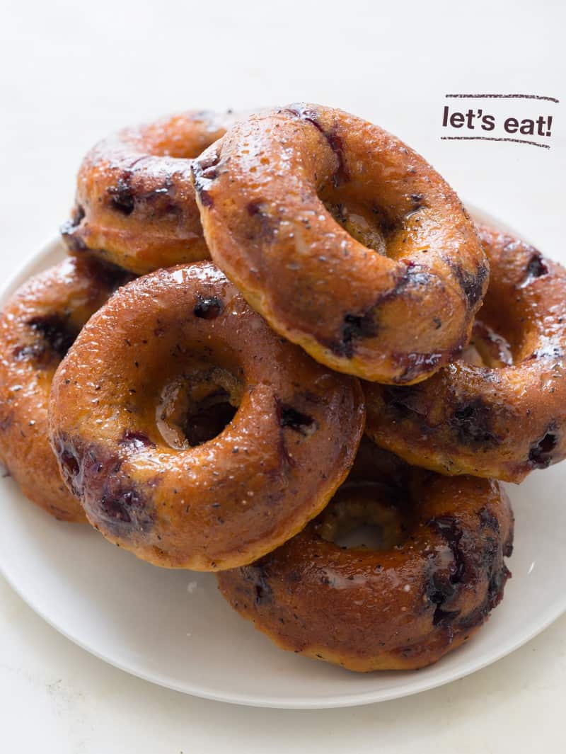 A pile of baked blueberry donuts on a white plate.