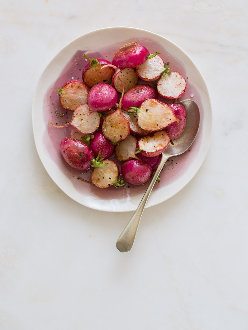 A bowl of roasted radishes with a spoon.