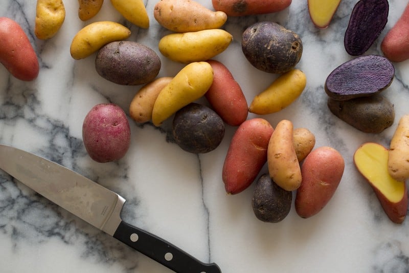 A close up of fingerling potatoes with a knife on a marble surface.