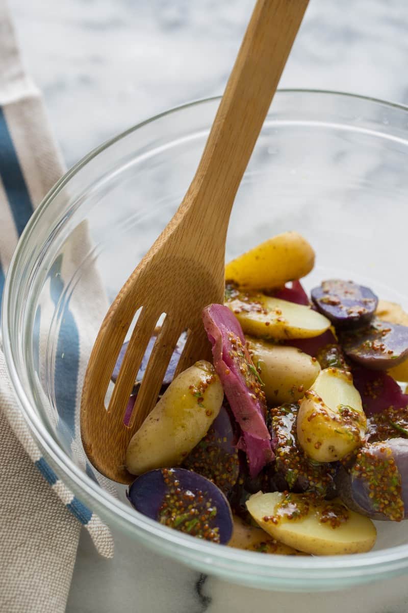 A close up of German potato salad being mixed in a bowl with a wooden spoon.