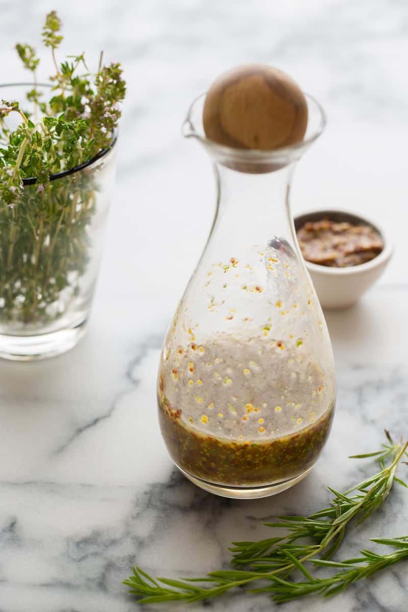 A close up of a bottle of mustard vinaigrette next to fresh herbs mustard.