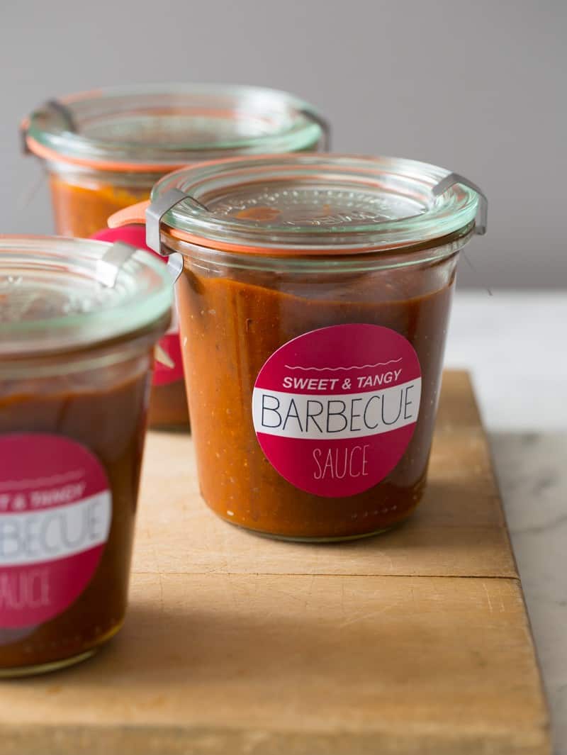 Labeled glass jars of sweet and tangy BBQ sauce on a wood surface.