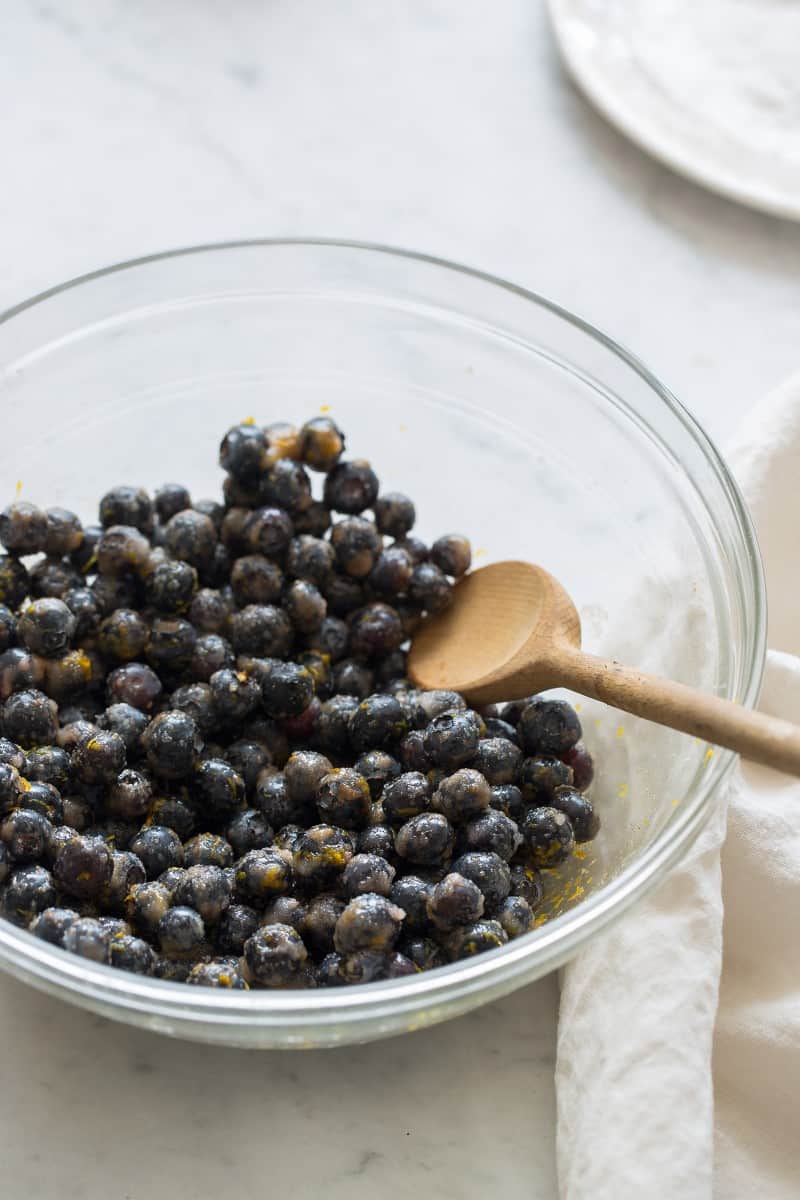 Blueberry Slab Pie filling A bowl of blueberries with a wooden spoon.