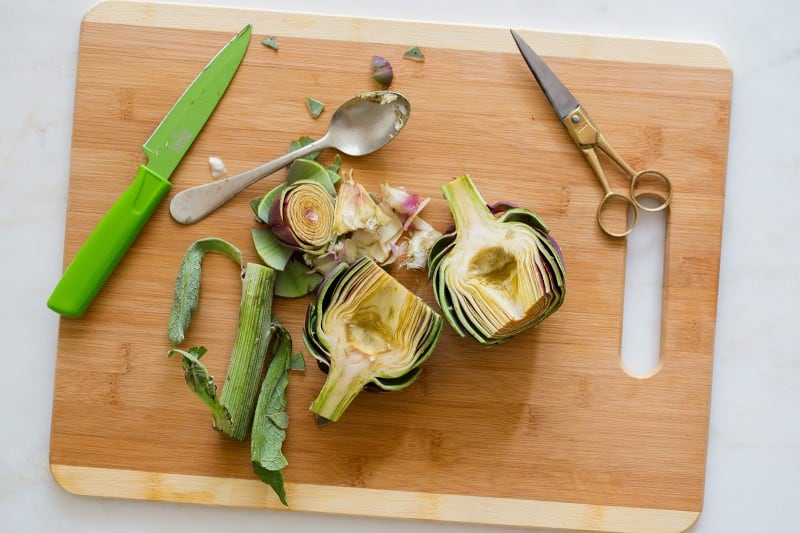 An artichoke cut in half and cleaned with a spoon, knife and scissors.
