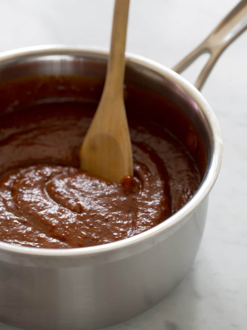 A pot of sweet and tangy BBQ sauce being stirred by a wooden spoon.