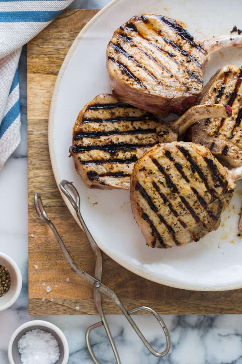 A close up of a plate of mustard crusted pork chops with serving tongs.