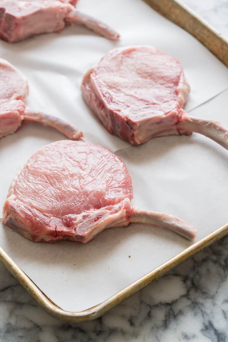 A close up of raw pork chops paid out on a sheet pan.