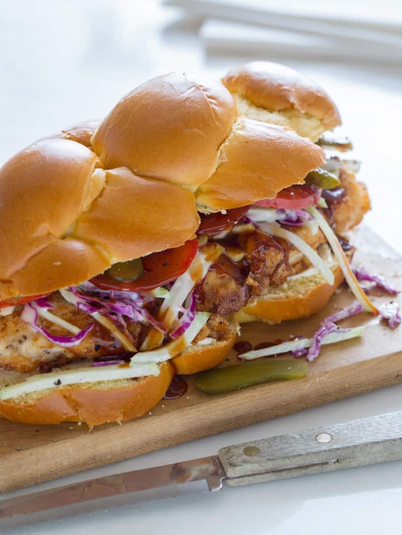 A fried chicken sandwich on a wooden board with a knife.