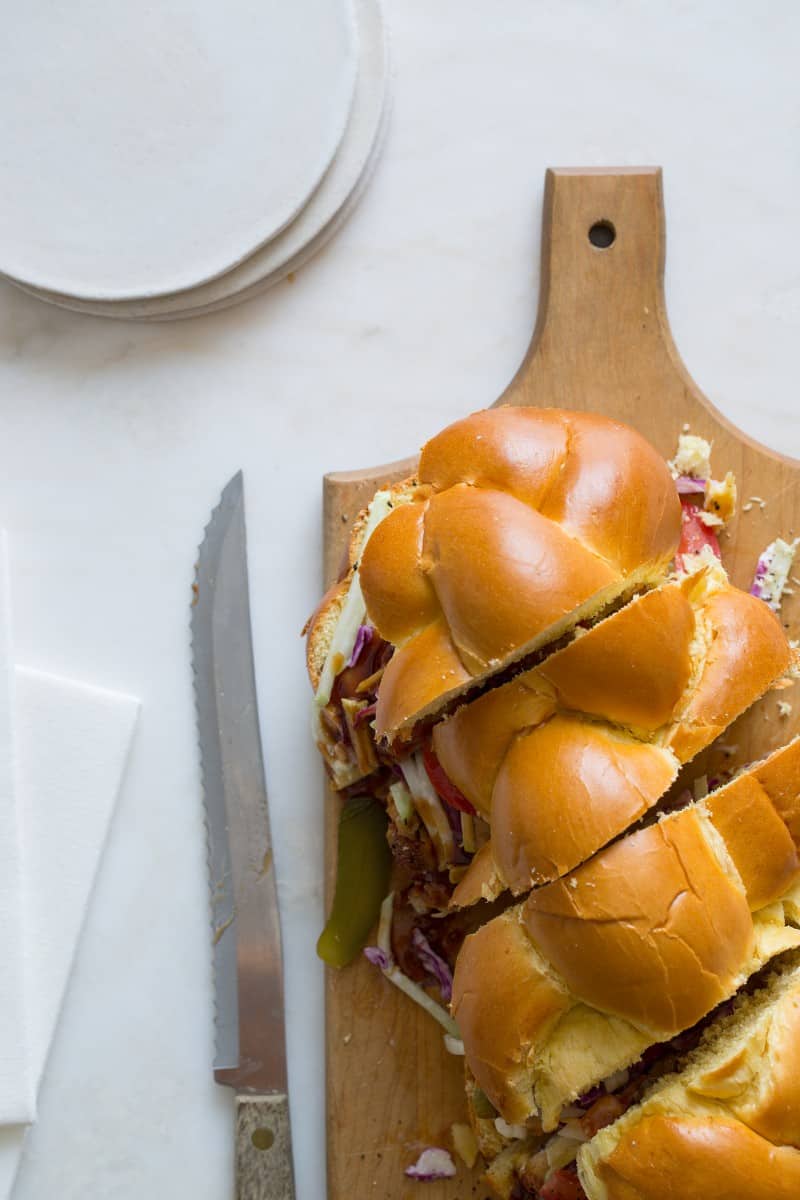 A sliced fried chicken sandwich on a wooden board with a knife and plates.