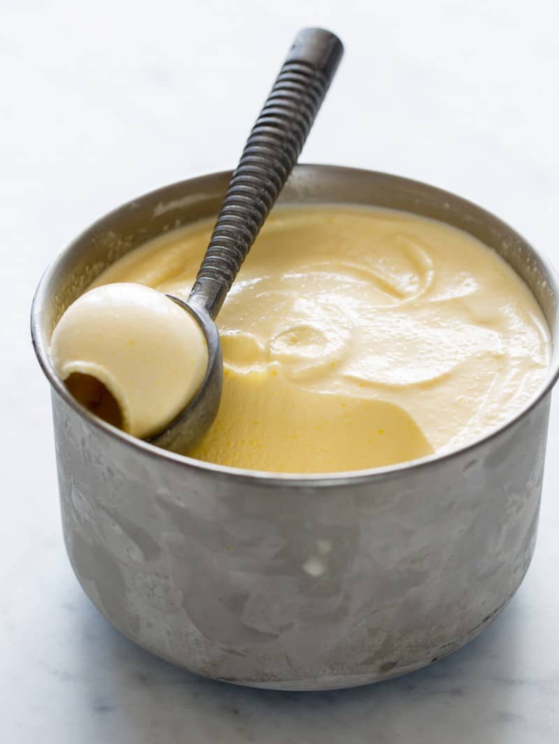 A bowl of sweet corn ice cream with a scooper full of ice cream.