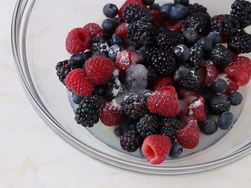 A close up of fresh berries and sugar in a mixing bowl.