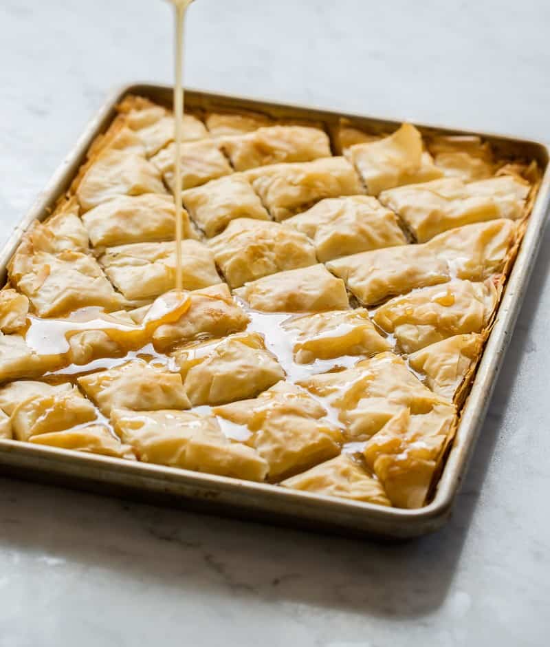 A tray of brie filled baklava with honey being poured over the top.