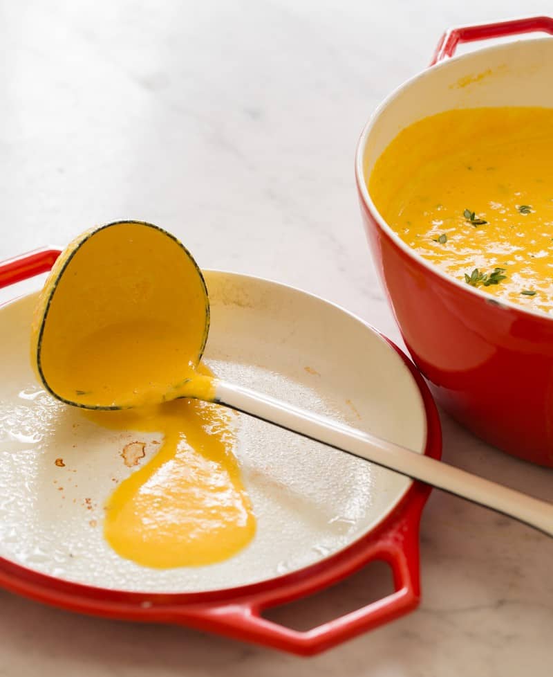 A pot of pumpkin beer cheese soup with a soup covered ladle on the pot lid.