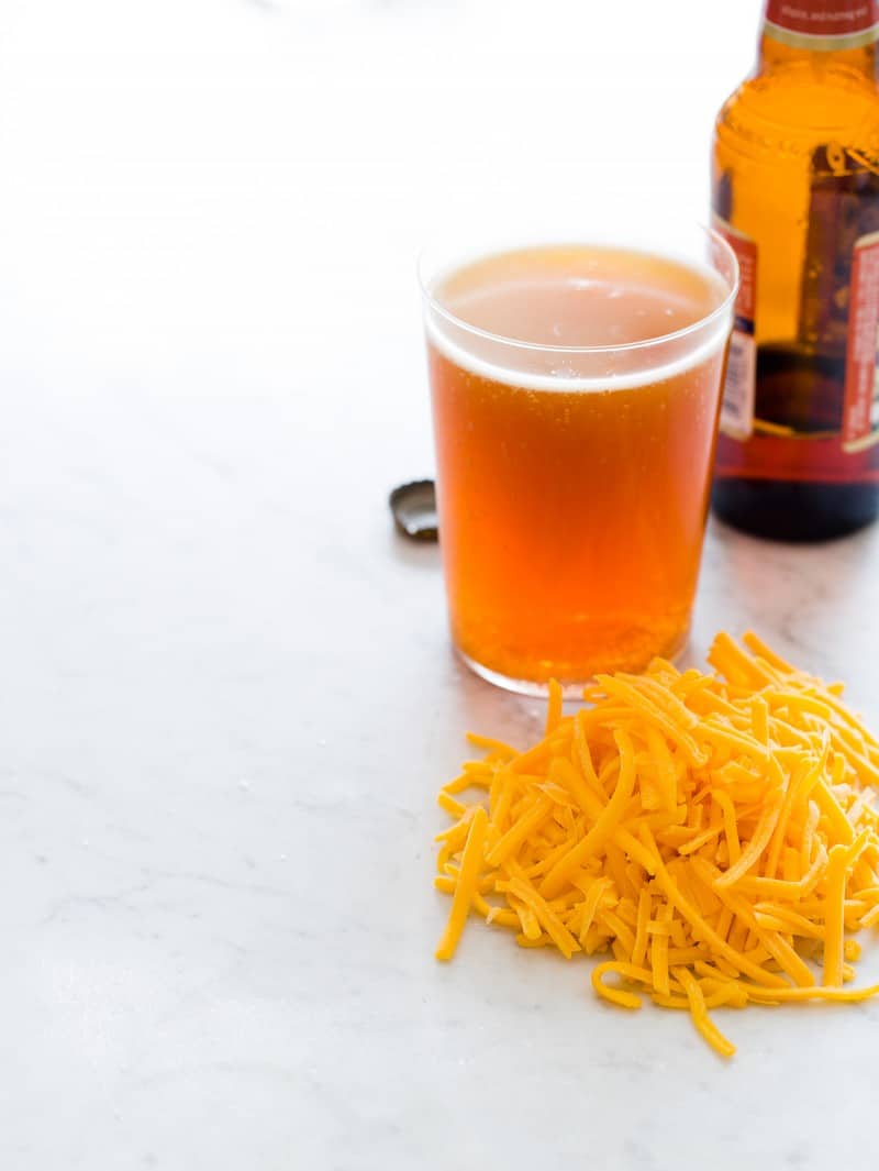 A glass and a bottle of beer next to a pile of shredded cheese.