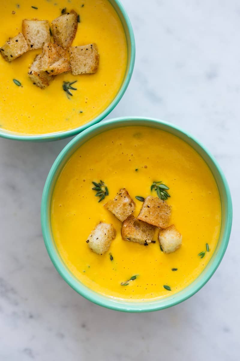 Overhead view of bowls of pumpkin beer cheese soup with croutons and thyme.