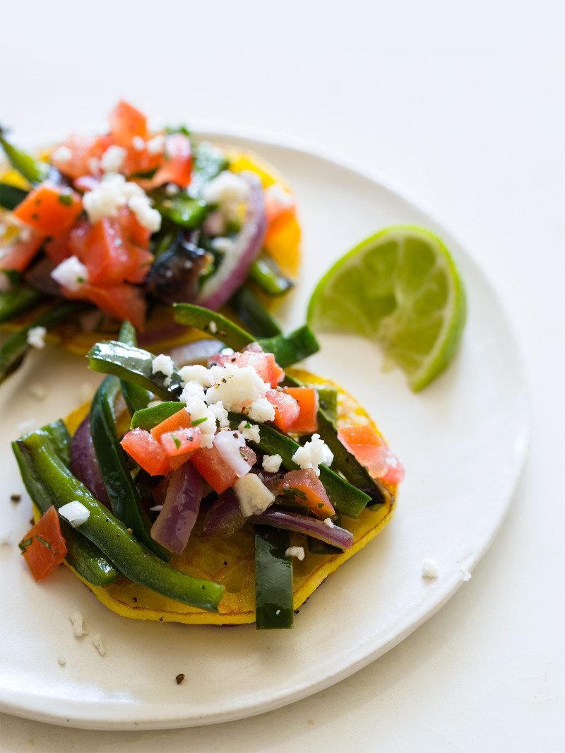 A close up of a plate cachapas topped with veggies and a lime wedge.