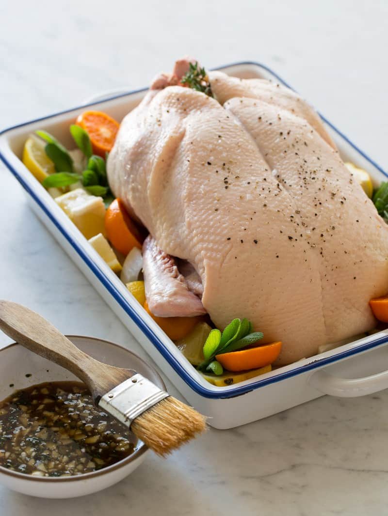 Maple Balsamic Roasted Duck recipe A raw duck with citrus and herbs with a bowl of maple balsamic and a brush.