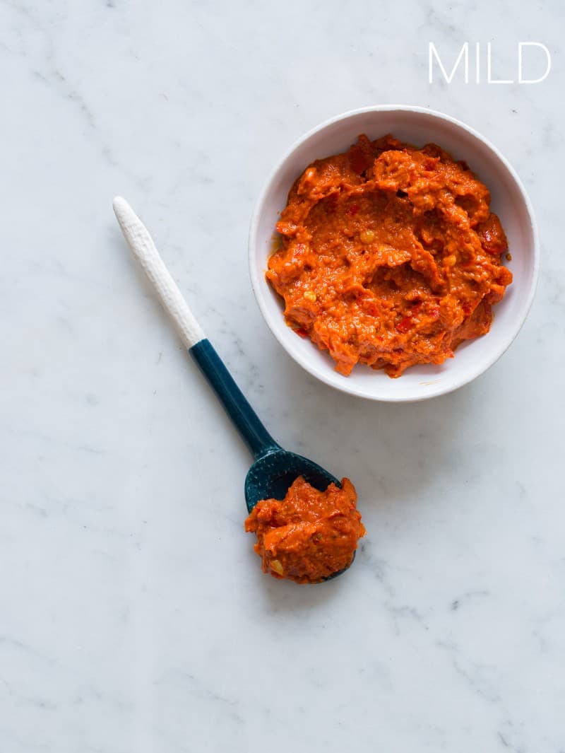 A blue and white spoonful of harissa next to a white bowl full of mild harissa.