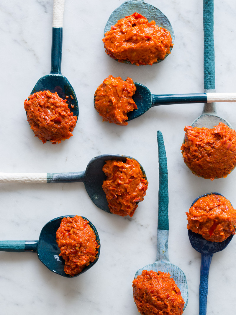 A close up of spoonfuls of harissa made two ways on several blue toned spoons.