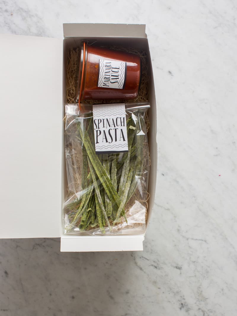 Clear labeled bag of homemade pasta with a labeled jar of sauce in a gift box.