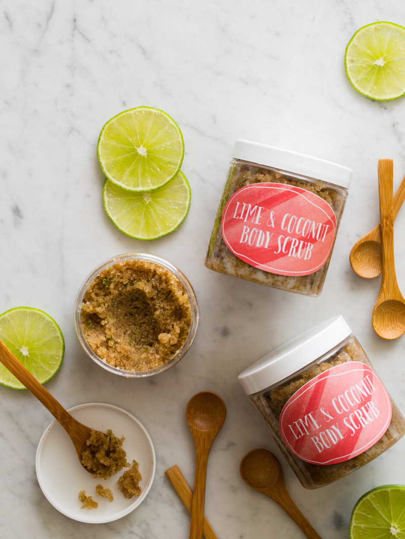 Lime and coconut body scrub in labeled containers with lime wheels and wooden spoons.