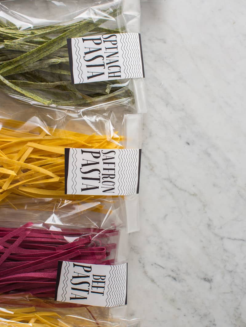 Clear labeled bags of homemade pastas lined up on marble surface.