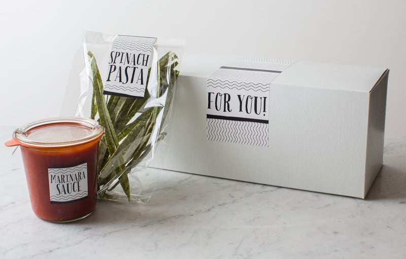 Labeled bag of homemade pasta with a labeled jar of sauce next to a gift box.