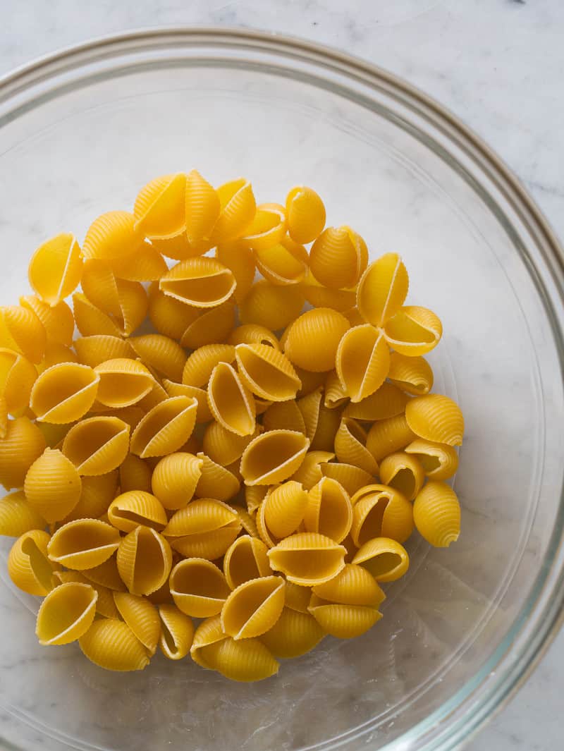 A glass bowl full of uncooked shell noodles for creamy skillet mac and cheese.