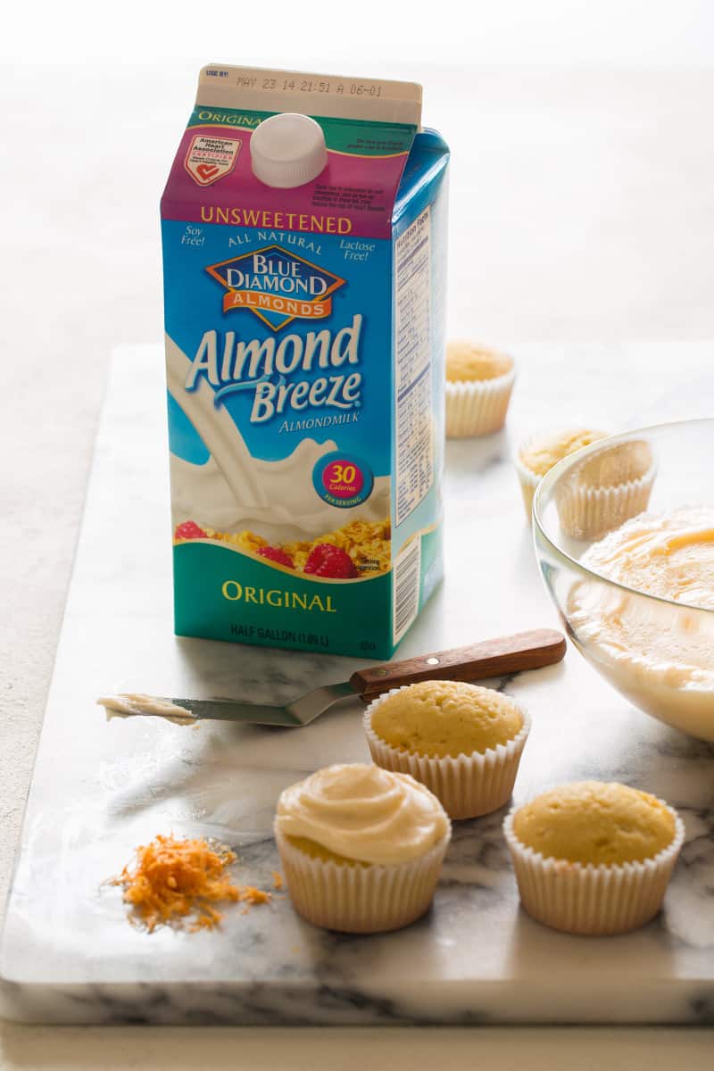 A carton of Blue Diamond almond milk next to butter cupcakes being frosted.