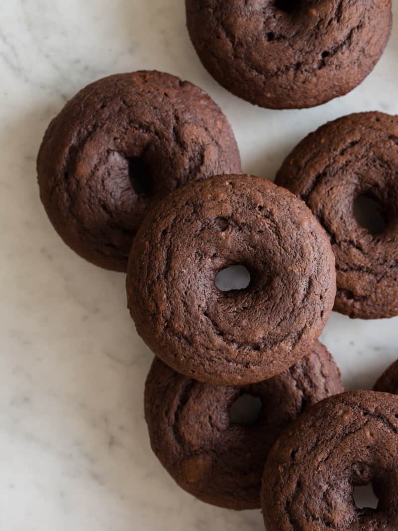 A close up of baked chocolate doughnuts on a marble surface.