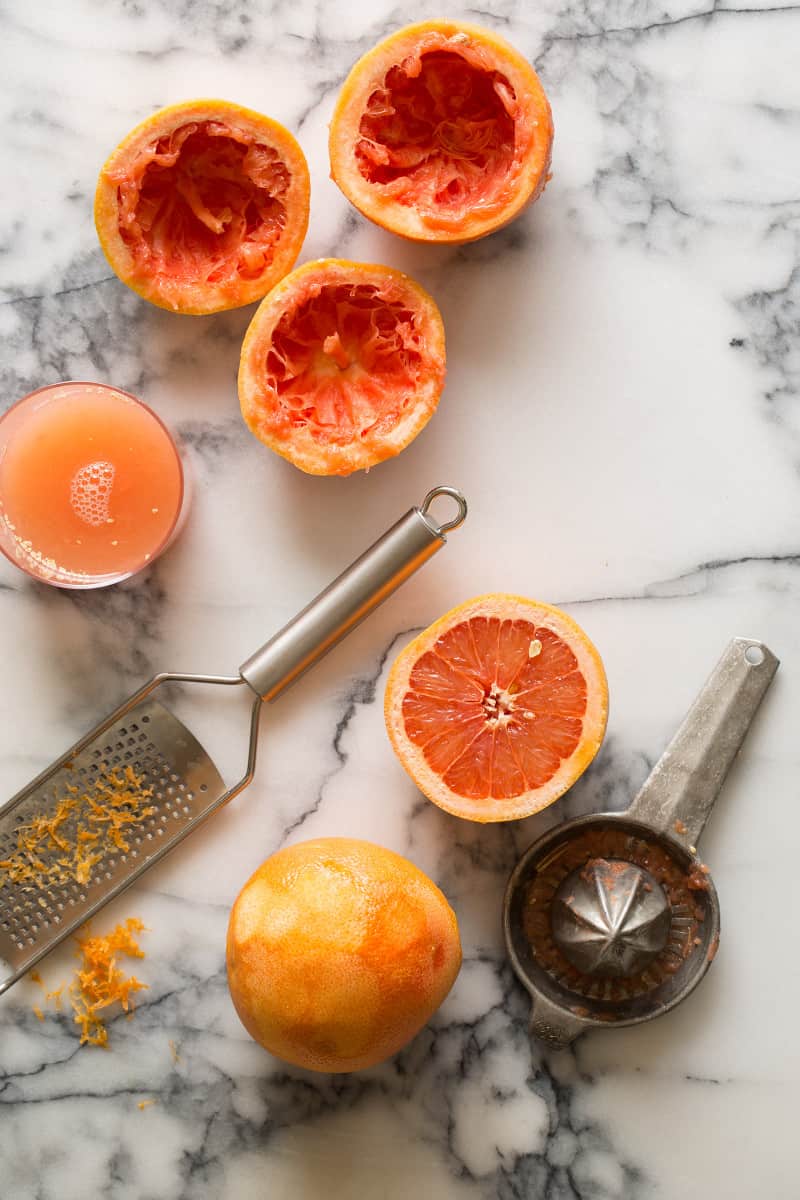 Grapefruit halves with a microplane and zest with a citrus juicer and a glass of juice.