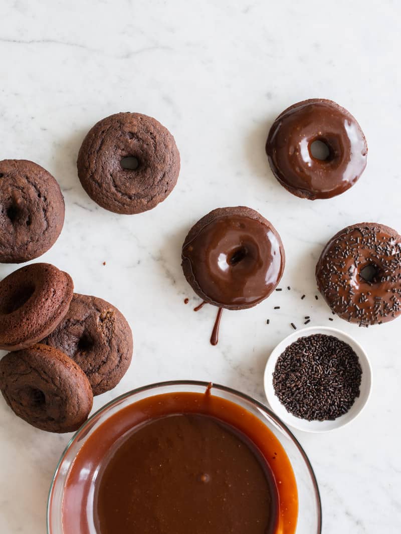 Baked Chocolate Doughnuts with Chocolate Frosting A bowl of frosting with baked chocolate doughnuts being frosted and sprinkled.