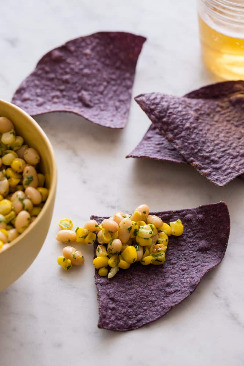 A bowl of white bean and corn salsa with some blue corn tortilla chips.