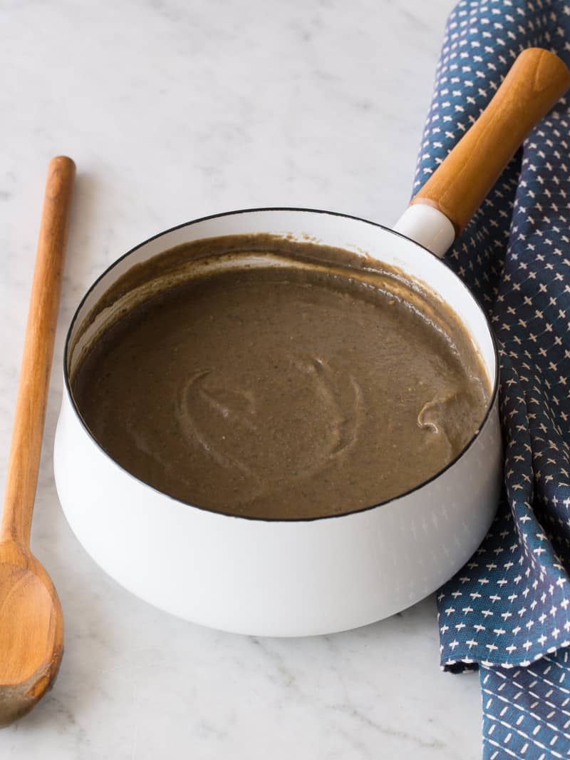 A pan of spicy black bean soup with a wooden spoon and linens.