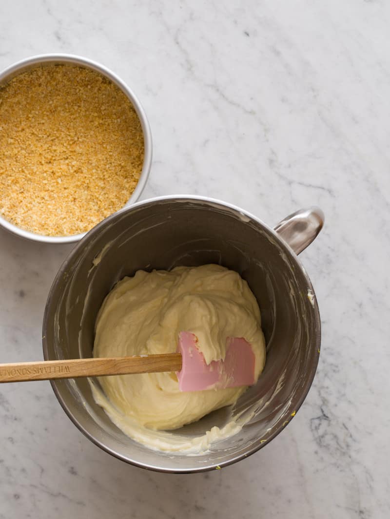 A pan with crust in place next to a bowl of cheesecake filling and a spatula.