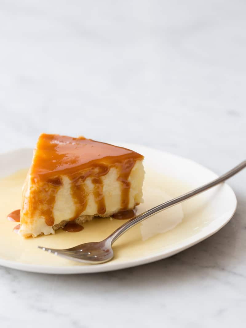 A piece of New York style cheesecake with cajeta drizzled on top with a fork.